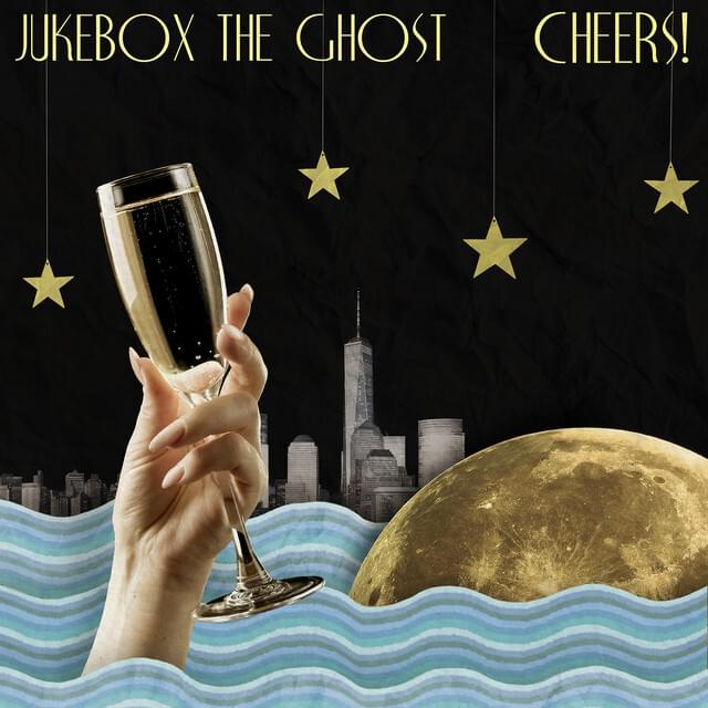 Black background with New York City skyline in the background; cartoonish water in the foreground. A giant moon sits in the water and a hand holding some champagne in a glass is on the left in th foreground of the picture. Text at the top in stylized gold reads: "Jukebox the Ghost, Cheers"