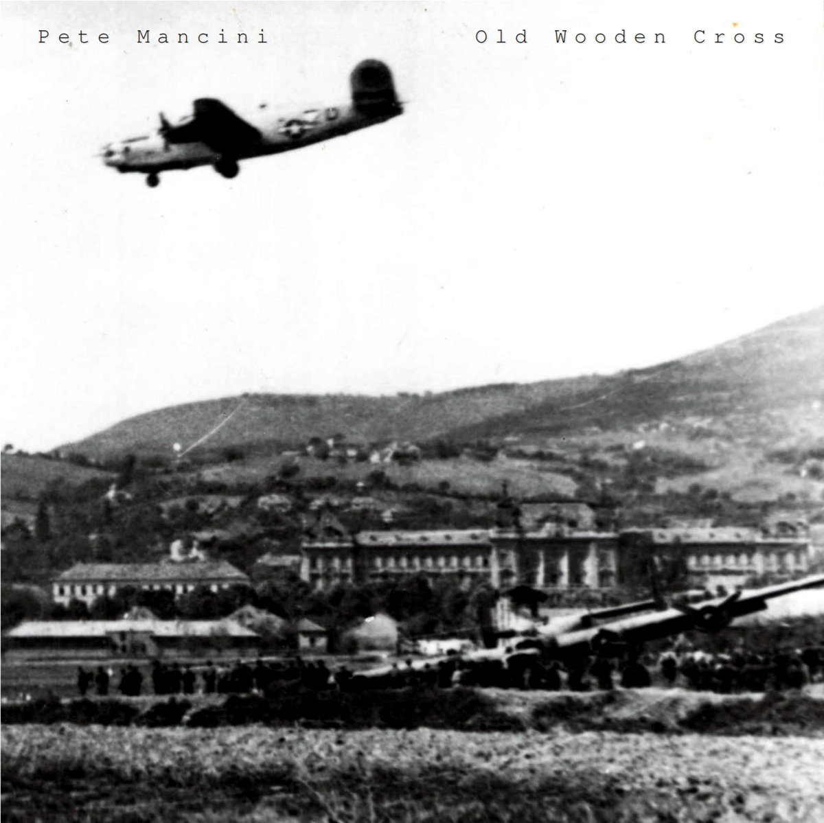 Black and white photo of a World War II era plane, descending over a town that looks to be likely based in Europe.