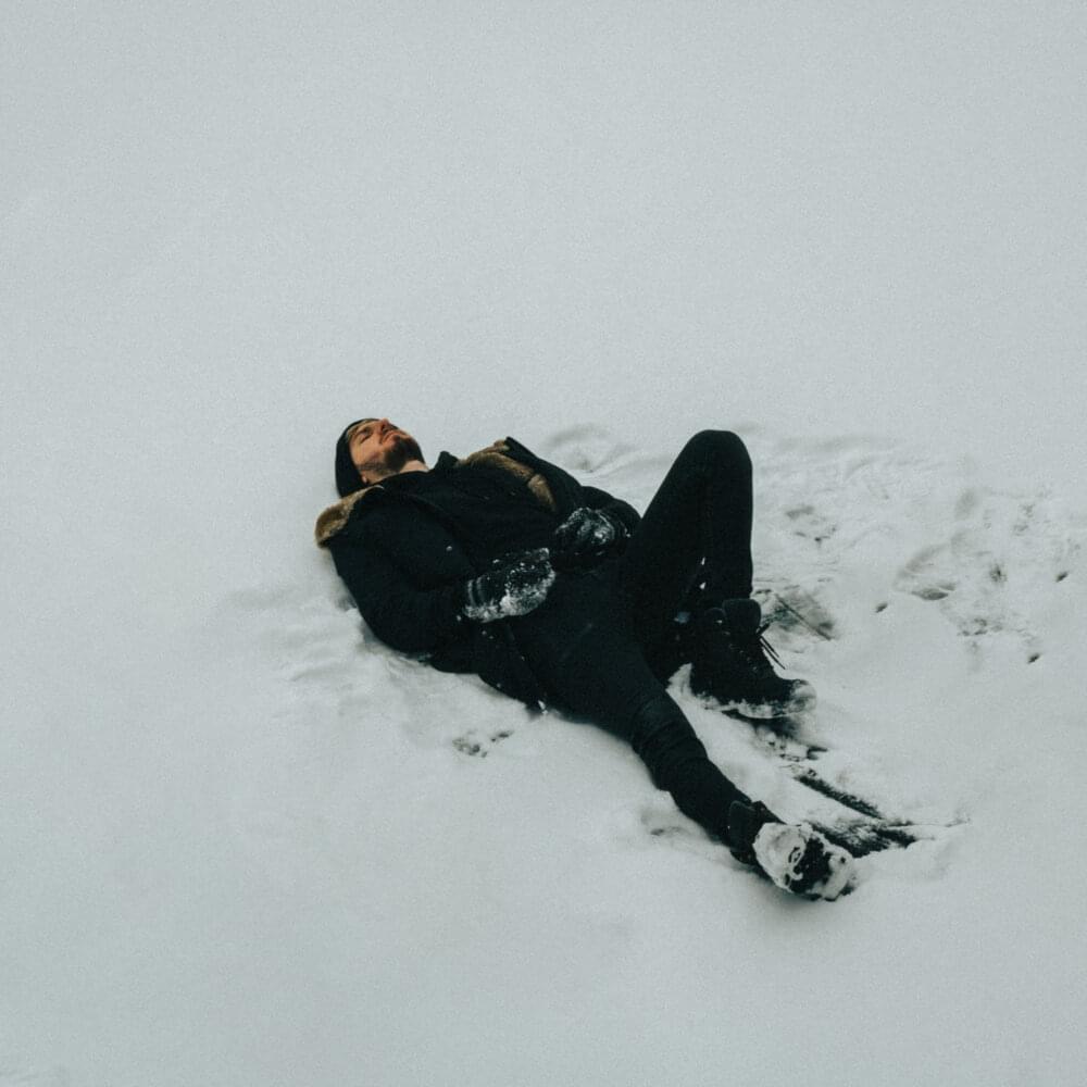 Man in black clothing, laying on his back in the snow